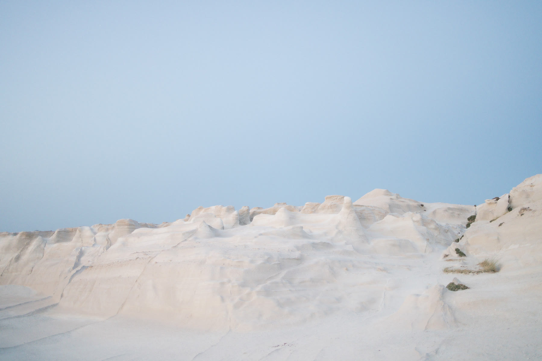 A tranquil landscape features smooth, white rock formations under a clear, pale blue sky.